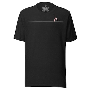 May include: Dark gray t-shirt with a minimalist design. A thin, horizontal line bisects the shirt, with a small, pink figure on the right side. The shirt has a crew neck and short sleeves. The upper left corner has a small tag.