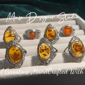 K&ouml;nnte beinhalten: Sechs Silberringe mit ovalen Bernstein-Edelsteinen. Die Ringe haben komplizierte Filigranarbeiten. Der Text "Muse Designer Studio" und "Real Gemstone, HandCrafted With Love" ist im Bild sichtbar.