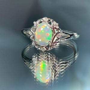 Könnte beinhalten: Ein silberner Ring mit einem ovalen Opal-Edelstein, der von kleineren klaren Steinen umgeben ist.