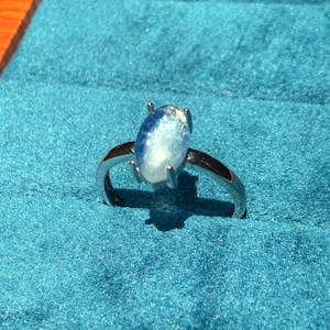 May include: A silver ring with a blue oval-shaped gemstone. The ring is set on a blue velvet background.