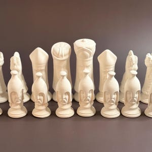 Puede incluir: Un juego de ajedrez completo con piezas blanquecinas. El conjunto incluye peones con diseño de casco, torres, caballos, alfiles, y un rey y una reina. Las piezas están dispuestas sobre un fondo liso, mostrando el juego completo.