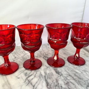 Puede incluir: Cuatro copas de vidrio rojo con un diseño texturizado. Las copas están sobre una superficie de mármol blanco.