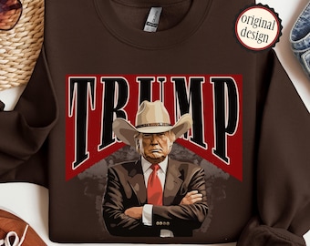 Könnte beinhalten: Braunes Sweatshirt mit einem Aufdruck eines Mannes mit Cowboyhut und Anzug. Der Aufdruck lautet "TRUMP" in großen, fetten Buchstaben.