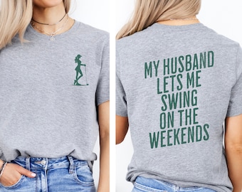 May include: Gray t-shirt with a green silhouette of a woman golfing on the front and the text "MY HUSBAND LETS ME SWING ON THE WEEKENDS" on the back.