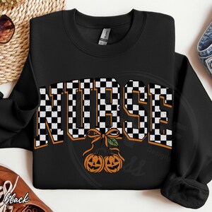 Puede incluir: Una sudadera negra de manga larga con la palabra NURSE en un patr&oacute;n de cuadros blancos y negros con un borde naranja. Debajo del texto hay un gr&aacute;fico de dos calabazas de Halloween naranjas unidas por un tallo con un lazo y una hoja verde.