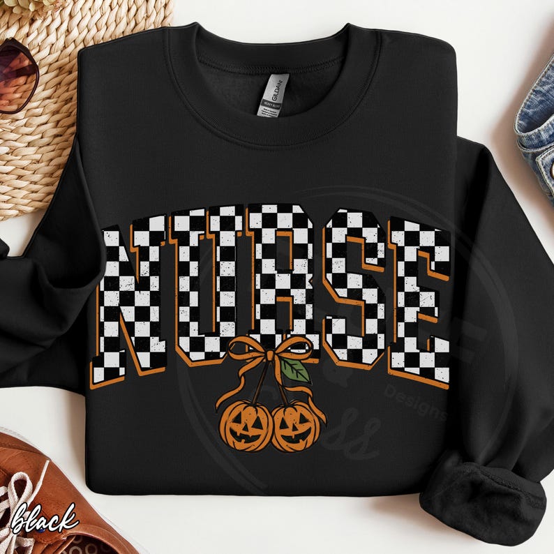Puede incluir: Una sudadera negra de manga larga con la palabra NURSE en un patr&oacute;n de cuadros blancos y negros con un borde naranja. Debajo del texto hay un gr&aacute;fico de dos calabazas de Halloween naranjas unidas por un tallo con un lazo y una hoja verde.