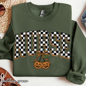 Puede incluir: Una sudadera de cuello redondo color verde oliva con la palabra NURSE en un patr&oacute;n de cuadros blancos y negros con bordes naranjas. Debajo del texto hay dos calabazas naranjas atadas con una cinta naranja y una hoja verde.