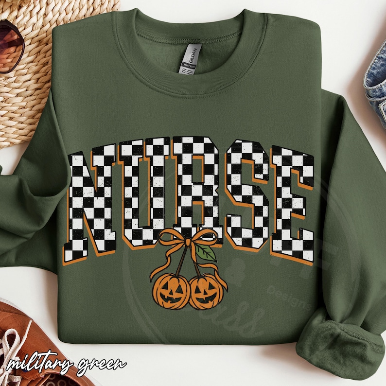 Puede incluir: Una sudadera de cuello redondo color verde oliva con la palabra NURSE en un patr&oacute;n de cuadros blancos y negros con bordes naranjas. Debajo del texto hay dos calabazas naranjas atadas con una cinta naranja y una hoja verde.