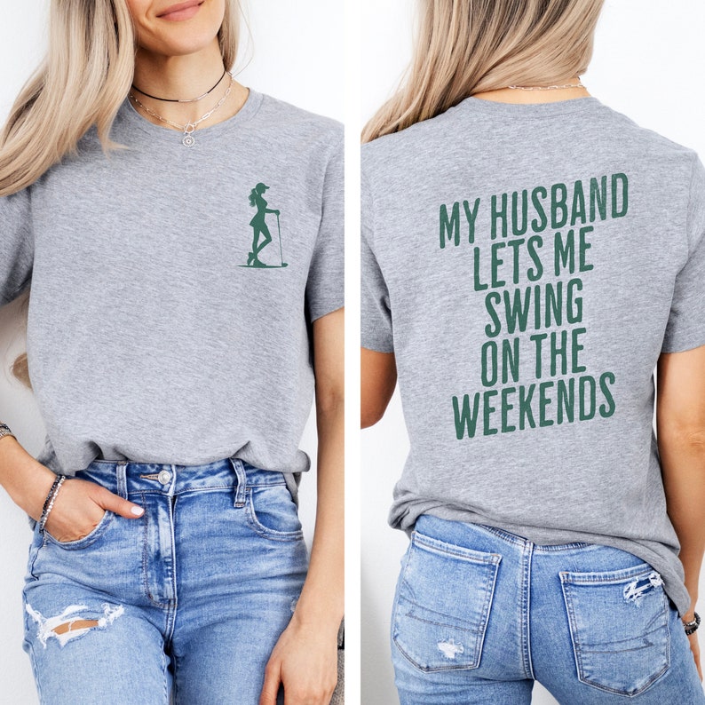 Może przedstawiać: Szara koszulka z zielonym sylwetowym wizerunkiem kobiety grającej w golfa z przodu i napisem "MY HUSBAND LETS ME SWING ON THE WEEKENDS" z tyłu.