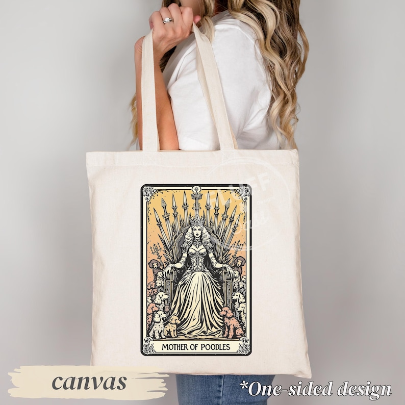 May include: Cream-colored canvas tote bag featuring a tarot card-style illustration. The design depicts a woman on a throne surrounded by poodles, with the text "MOTHER OF POODLES." The bag has long handles and the word "canvas" is printed on the bottom.