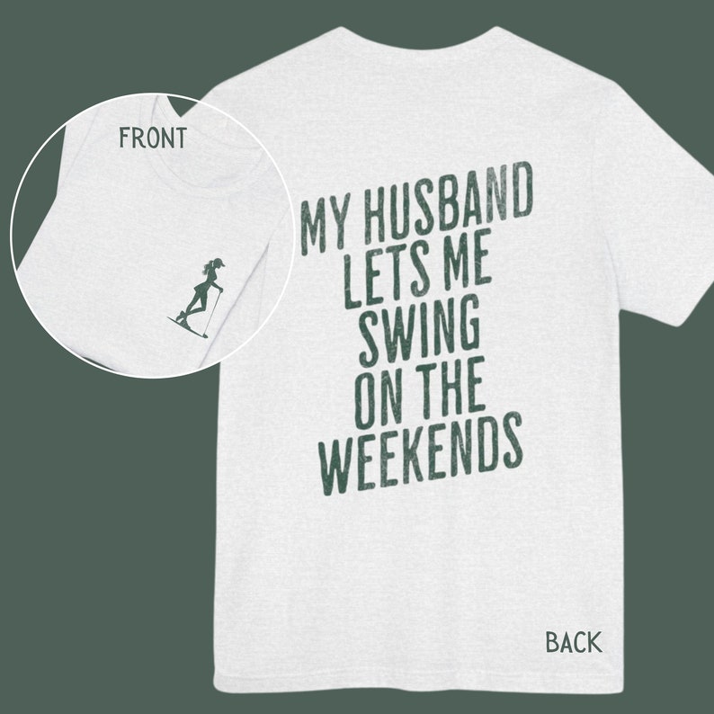 Może przedstawiać: Biała koszulka z nadrukiem "My husband lets me swing on the weekends" na plecach w ciemnozielonym kolorze. Prz&oacute;d koszulki ma mały grafik przedstawiający kobietę na nartach wodnych.