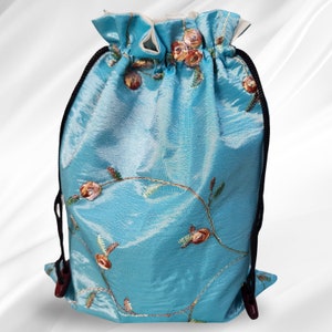 May include: A light blue drawstring bag with floral embroidery. The bag has a black drawstring and a white lining.