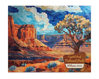 Op de afbeelding: Een kleurrijke mozaïekkunstprint die een woestijnlandschap weergeeft met rode rotsformaties, een boom en een blauwe lucht met wolken. De print bevat een bord met de tekst "Capitol Reef National Park Wilsons 2024."