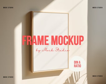 May include: A gold-framed mockup of a blank poster with the text "FRAME MOCKUP by Mock Studio" and "DIN A RATIO" in red. The poster is hanging on a light beige wall with shadows from sunlight.