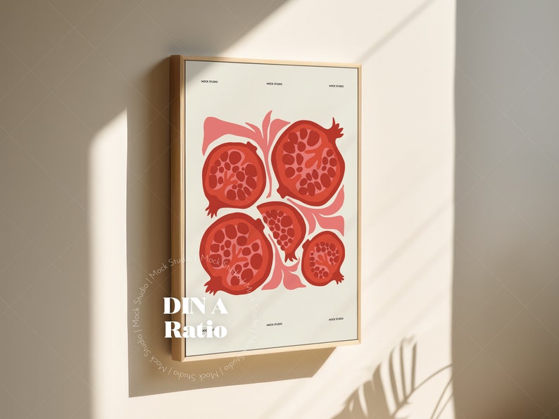 May include: A framed print with a white background and a design of five red pomegranate fruit slices. The text "DIN A Ratio" is printed in white at the bottom of the print.