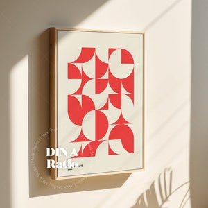 May include: A framed print with a geometric design featuring red and white shapes. The print is titled "DIN A Ratio" and is hanging on a white wall.