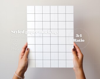 May include: A white sheet of paper with a grid pattern is held by two hands. The paper is 3:4 ratio. The text "Styled paper mock-up" is visible at the top of the paper. The text "Smart object" is partially visible below the text "Styled paper mock-up". The text "PSD, JPG, PNG" is visible below the text "Smart object".
