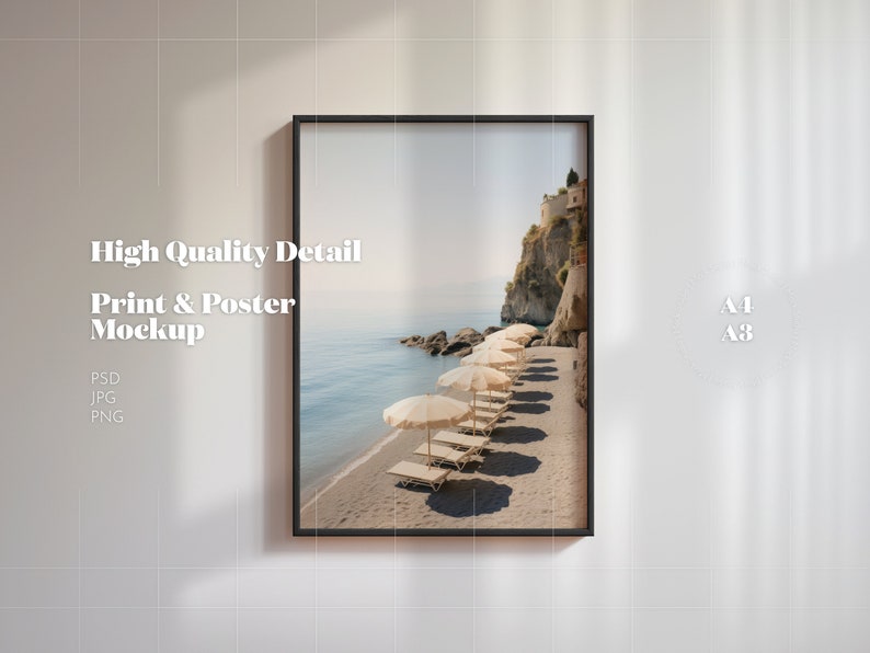 May include: A framed print mockup of a beach scene with white umbrellas and lounge chairs on a sandy beach. The beach is next to a rocky cliff with a small town on top. The print is in a black frame and is hanging on a white wall. The text "A1 A3" is visible in the upper right corner of the image.