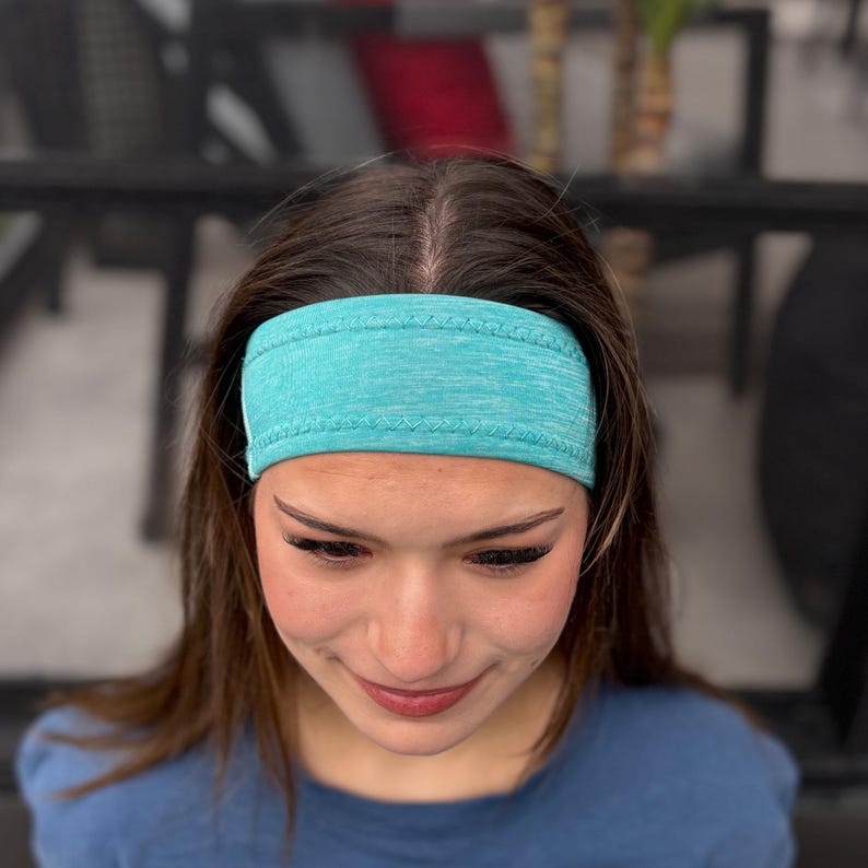 May include: A turquoise blue headband made of a soft, stretchy fabric. The headband is worn by a person with brown hair.