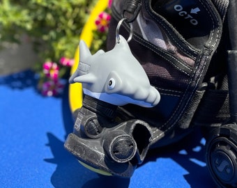 May include: A gray shark-shaped scuba diving mouthpiece attached to a black scuba diving regulator with a black and gray strap.