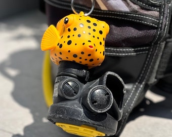 May include: A yellow and black pufferfish keychain attached to a black scuba diving regulator.