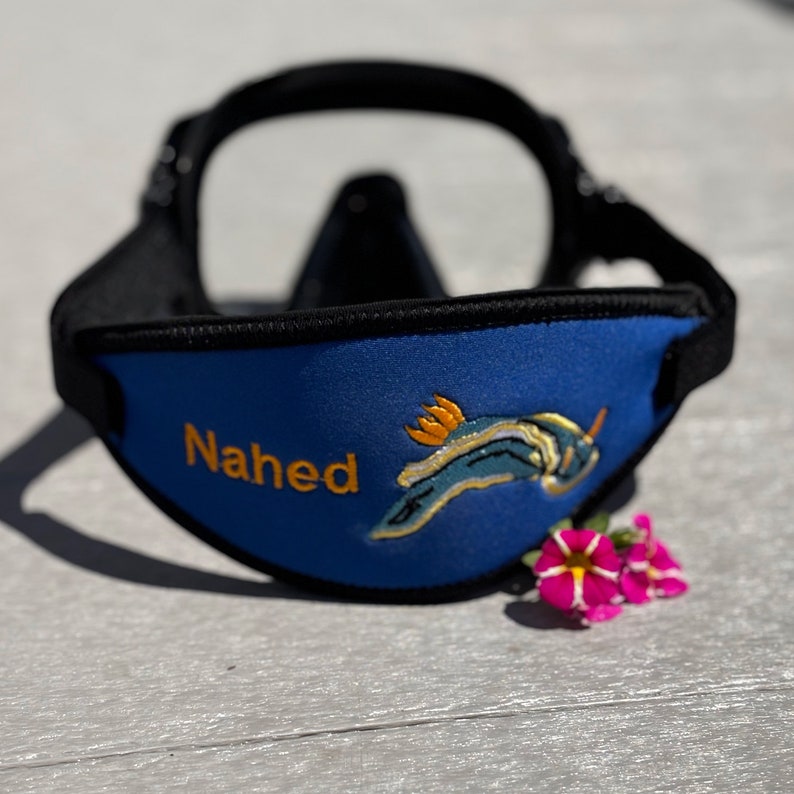 A blue neoprene swim mask with a black strap and a yellow and blue sea slug design. The mask is personalized with the name "Nahed".