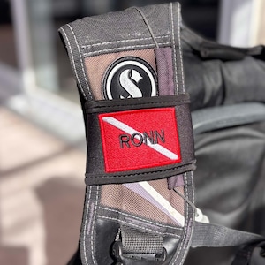 May include: A black scuba diving backpack with a red and white scuba diving flag patch that says "RONN" on it.