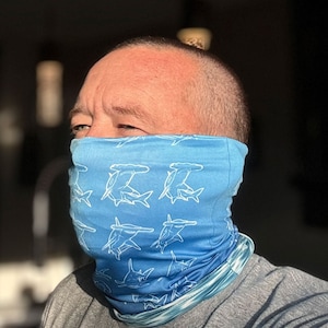 Pode incluir: Uma máscara facial azul com um padrão de tubarão martelo branco. A máscara está sendo usada por uma pessoa.