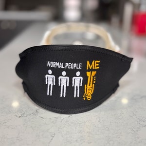 以下が含まれることがあります： 白文字と棒人間が特徴の黒いフェイスマスクで、「NORMAL PEOPLE」と「ME」が黄色で表示されています。「ME」は様式化された逆さまの姿です。マスクは鼻と口を覆うように設計されています。