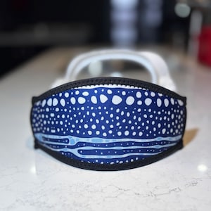 May include: A blue face mask with a white dot pattern and a black border. The mask has a curved shape and is designed to cover the nose and mouth. The mask has a light blue design at the bottom.