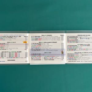 May include: A tri-fold card game with text and number combinations, displayed in a clear plastic sleeve. The card features various game titles and point values, with a green background.