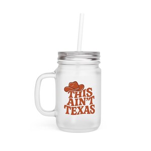 Questa tazza in barattolo di vetro "Aint Texas" è una tazza western smerigliata ispirata al tour Cowboy Carter, all'estetica country di Beyoncé e al cappello da cowgirl.