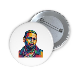 Könnte beinhalten: Ein weißer Button mit einem farbenfrohen Pop-Art-Porträt eines Mannes mit einer goldenen Kette. Das Porträt verwendet eine lebendige Palette aus Blau, Grün, Gelb und Rot. Ein zweiter Button ist teilweise sichtbar.