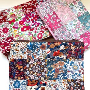 Puede incluir: Tres estuches con cremallera hechos de tela de patchwork con estampados florales en tonos rosa, rojo y azul. Los estuches están alineados en una fila, con el estuche rosa en la parte posterior, el estuche rojo en el medio y el estuche azul en la parte delantera.