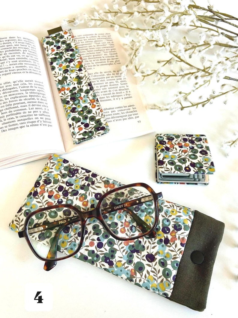 May include: An eyeglasses case, bookmark, and small notebook are shown. The case and bookmark have a floral pattern with green, blue, and purple flowers on a white background. The eyeglasses have a brown tortoiseshell frame.