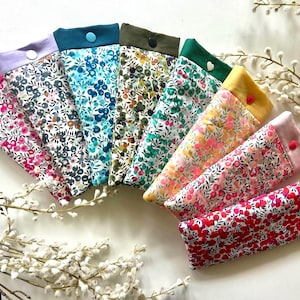 May include: A selection of fabric cases with floral patterns and solid-coloured tops. The cases are arranged in a fan shape, displaying a range of colours such as pink, blue, green, and yellow. Each case features a button closure.
