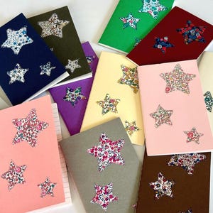 May include: A selection of notebooks in various colours, each featuring star-shaped cutouts filled with floral fabric. Notebooks include navy, pink, green, and brown. Each notebook has a unique floral pattern.