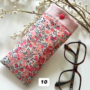 May include: A floral eyeglasses case with a pink top and a heart-shaped button. The case is next to a pair of brown, square-framed eyeglasses. The case has a pattern of pink and red flowers on a cream background. The number "10" is in the lower left corner.