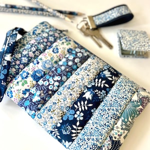 May include: A collection of blue floral accessories, including a quilted pouch, key fob, small square case, and pencils. The items feature various shades of blue and white floral patterns, creating a coordinated set.