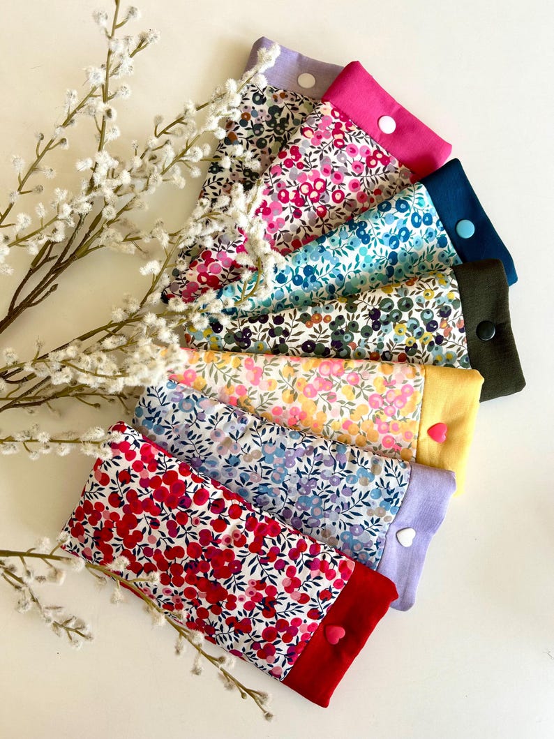 May include: A selection of fabric cases with floral patterns in shades of red, pink, blue, and yellow. Each case has a solid-colored border and a heart-shaped button. The cases are arranged with white floral sprigs in the background.