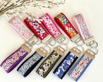 May include: A selection of keyrings with floral fabric straps in shades of pink, red, purple, and blue. Each keyring features a silver-tone metal clasp and ring.