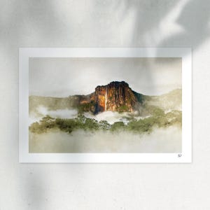 Può includere: Una stampa paesaggistica che mostra un'alta scogliera scura con una sottile cascata che scende lungo il centro. La base della montagna è circondata da una fitta foresta verde e da spesse nuvole bianche, con una piccola firma nell'angolo in basso a destra.