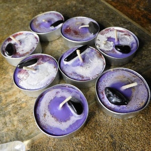 May include: Purple and white tea light candles with black stones embedded in the wax. The candles are in a silver holder.