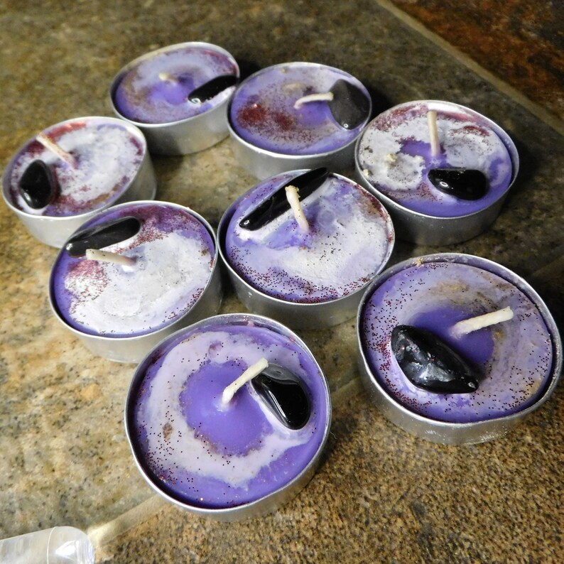May include: Purple and white tea light candles with black stones embedded in the wax. The candles are in a silver holder.