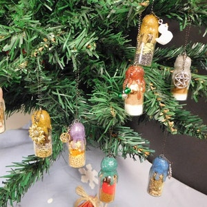 May include: A collection of eight glass bottle ornaments, each filled with different materials and topped with a decorative charm. The ornaments are hanging from a green artificial Christmas tree.