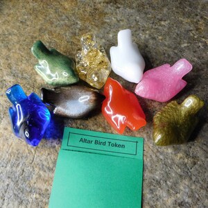 May include: A set of nine colorful bird-shaped resin tokens with a green card that reads "Altar Bird Token". The tokens are in various colors, including blue, green, red, brown, white, gold, and pink.