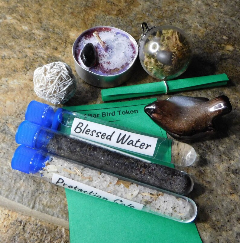 May include: A green card with the text "Star Bird Token" and "Blessed Water" on it. There are three test tubes with blue caps, one filled with salt, one with water, and one with a dark substance. There is a small white crystal, a brown ceramic bird, a green glass orb, and a purple candle.