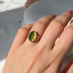 May include: A gold ring with a large oval green gemstone. The ring is on a finger.