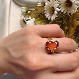 May include: A gold ring with a large oval-shaped orange gemstone. The ring is set in a delicate gold band.
