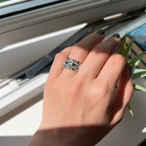 May include: A hand wearing a set of four silver rings with green gemstones. The rings are stacked on each other and have a delicate design.